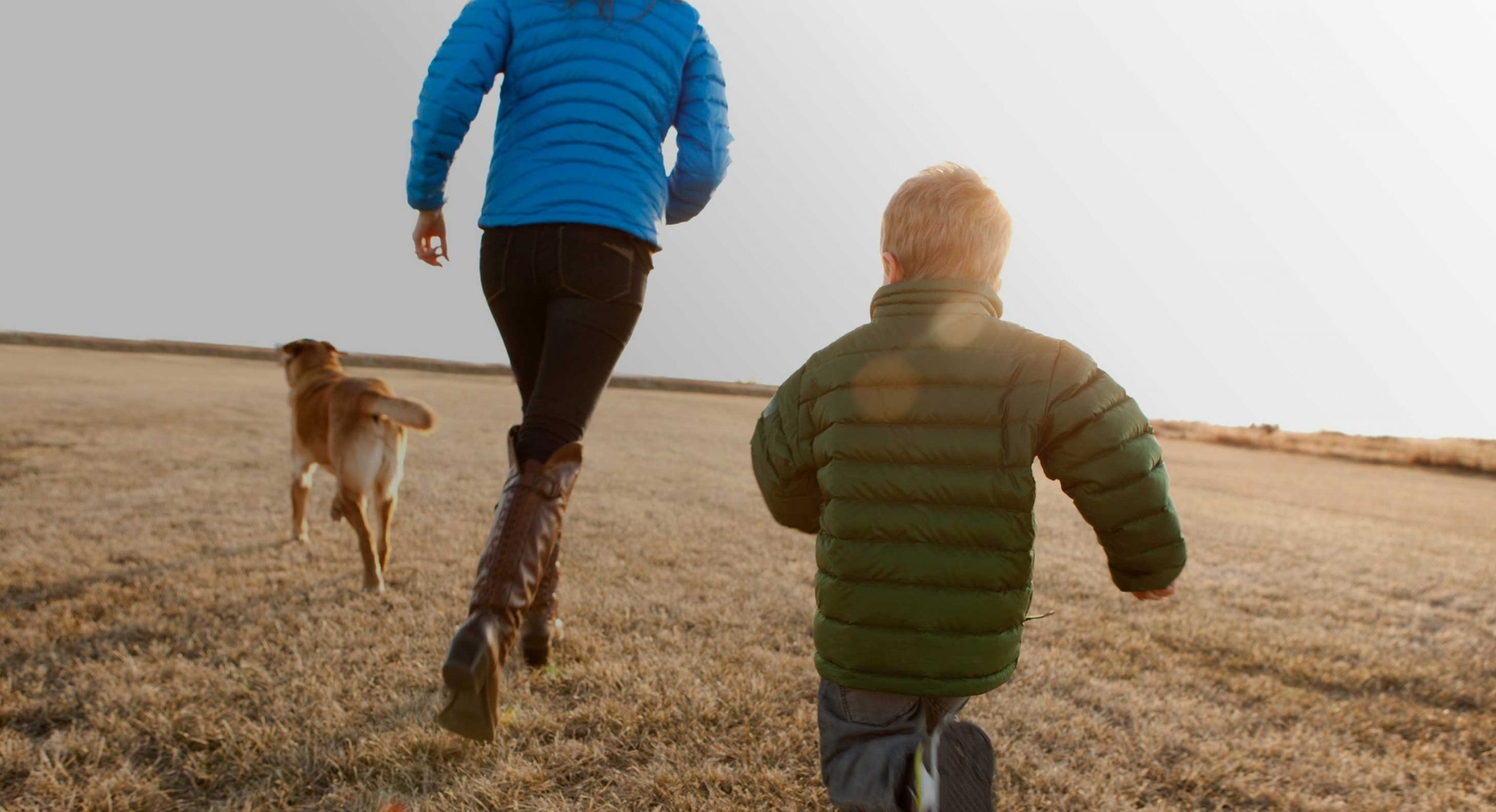 Aetna hero image - parent, child and family dog running through a field