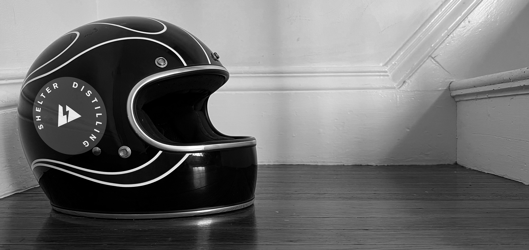 Motorcycle helmet with Shelter Distilling logo on it photographed in black and white, positioned at the bottom of stairwell