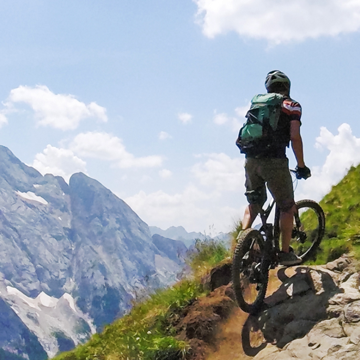 A person riding a mountain bike near the edge of a cliff, dramatic mountain view in the background