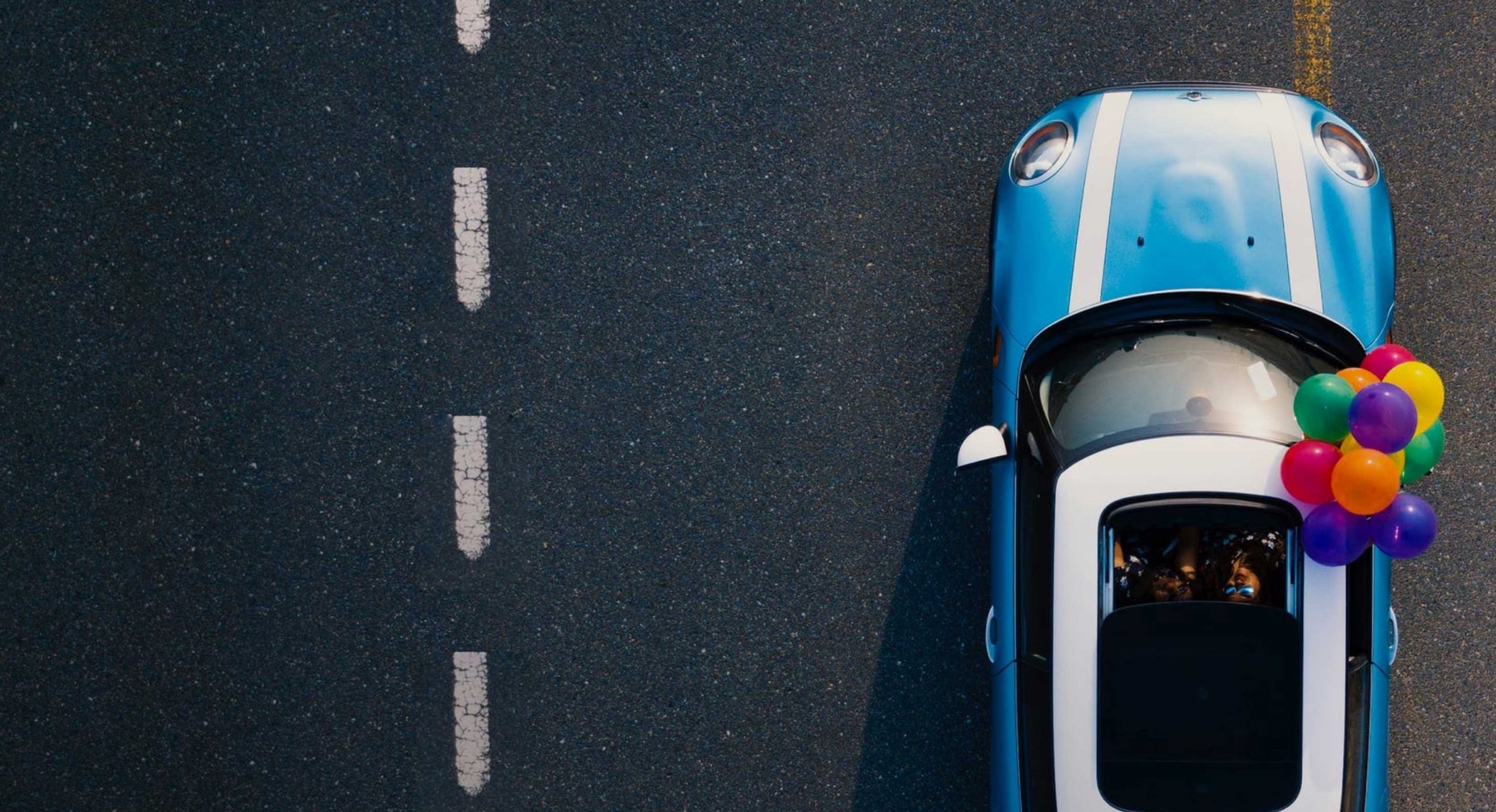 Blue Mini Cooper driving on a road with balloons hanging out passenger window