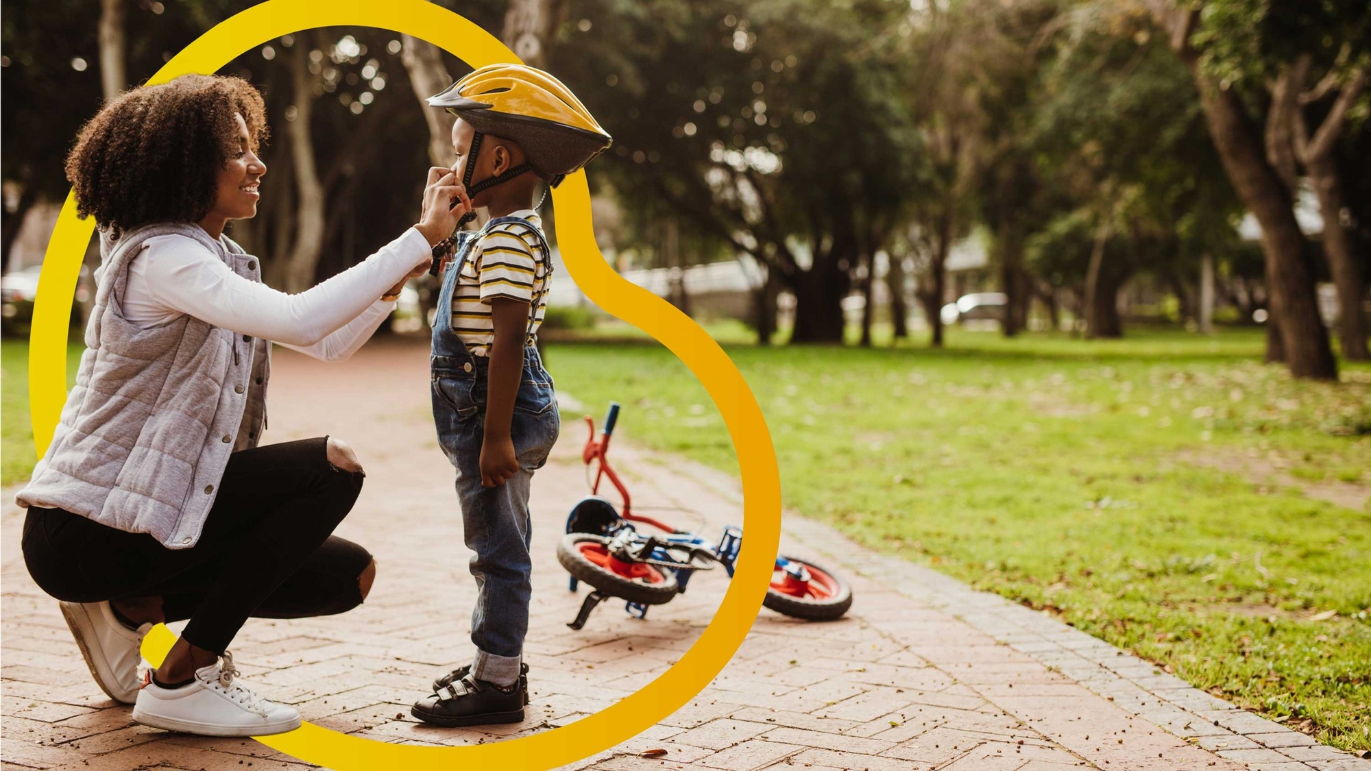 Goldfinch design mock up - woman tightening child's bike helmet in park with Goldfinch logo atop