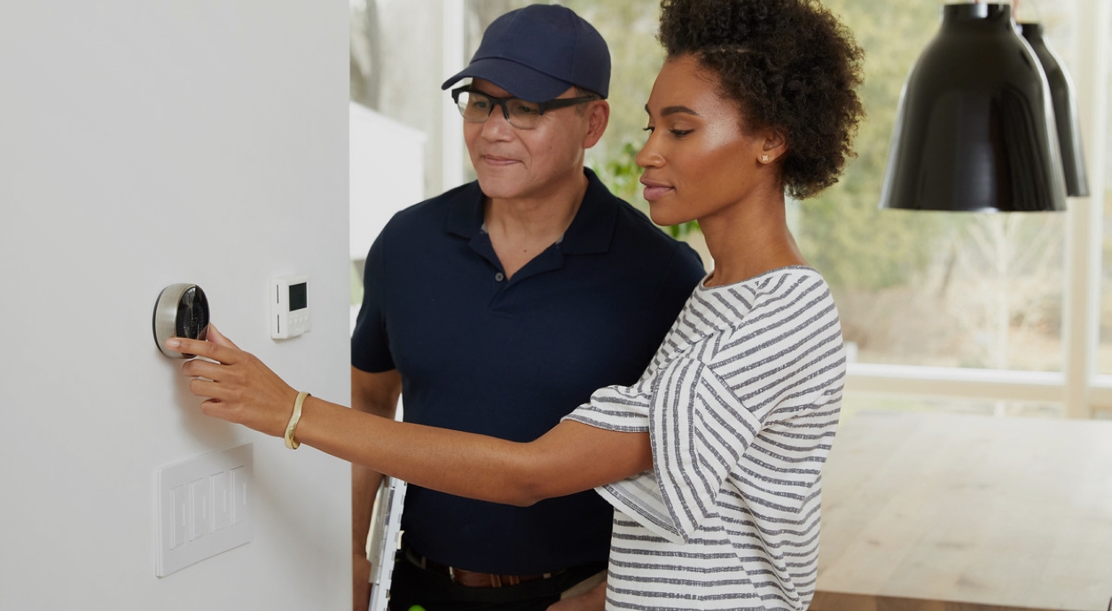 A home repair person helping a woman setup and adjust thermostat